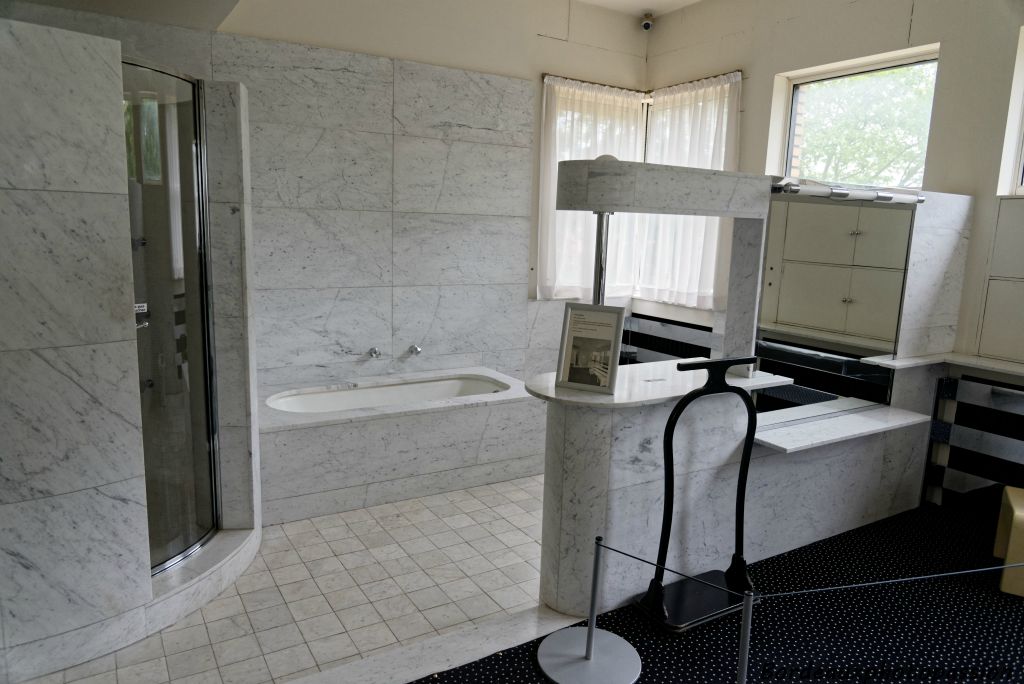 Une zone comprenant la douche et la baignoire avec séparation en épi réalisée en marbre blanc et cuivre chromé.